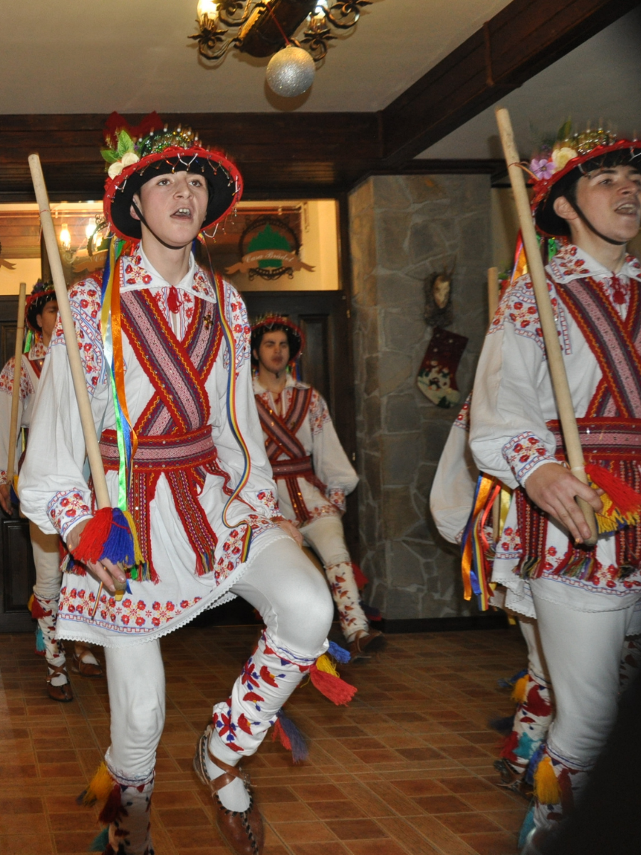 Tineri în costum de iarnă dansând cu bâte de lemn la Casa Brădet