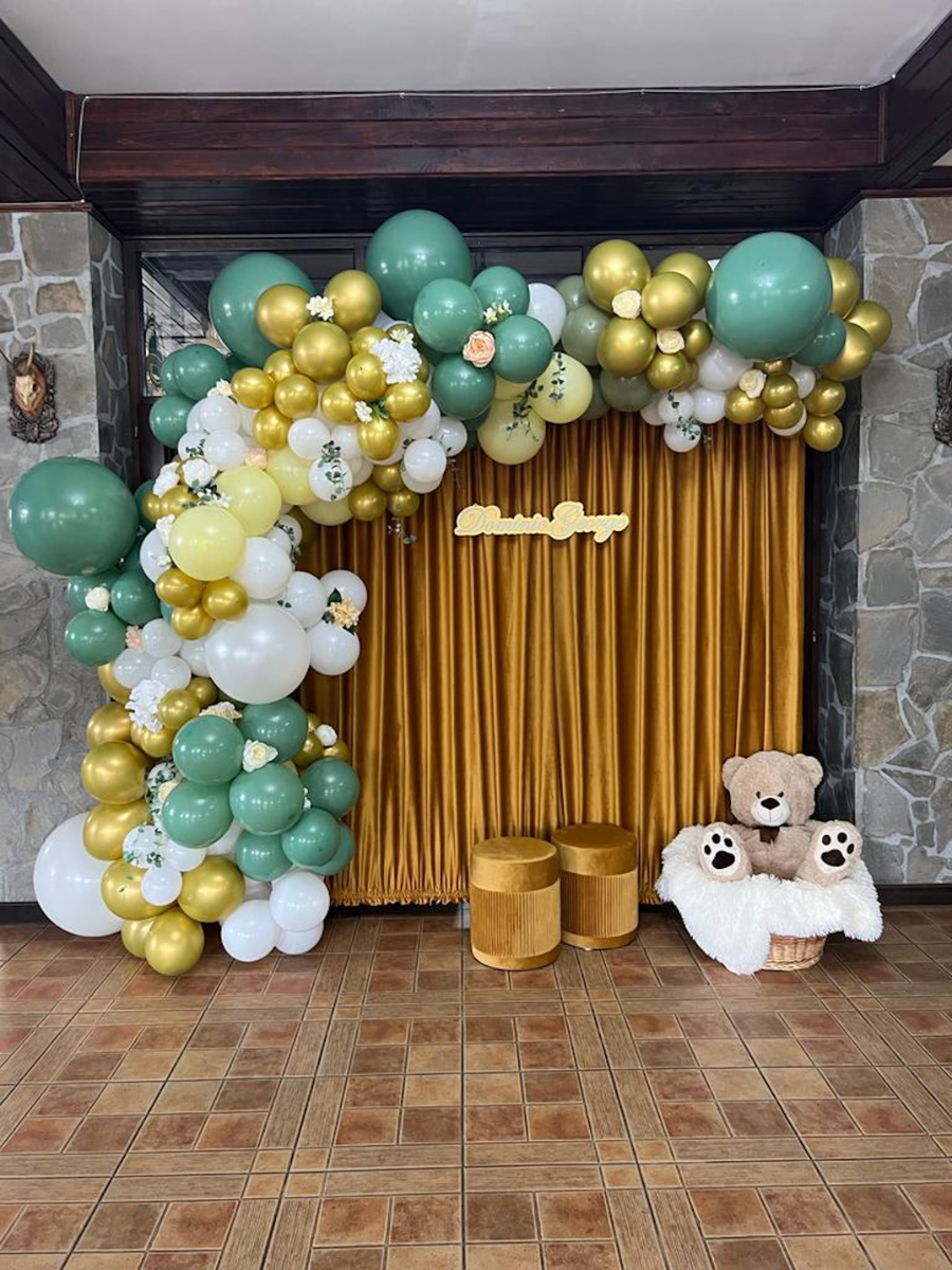 Colț foto cu arcadă de baloane verde-auriu și draperie galbenă la eveniment