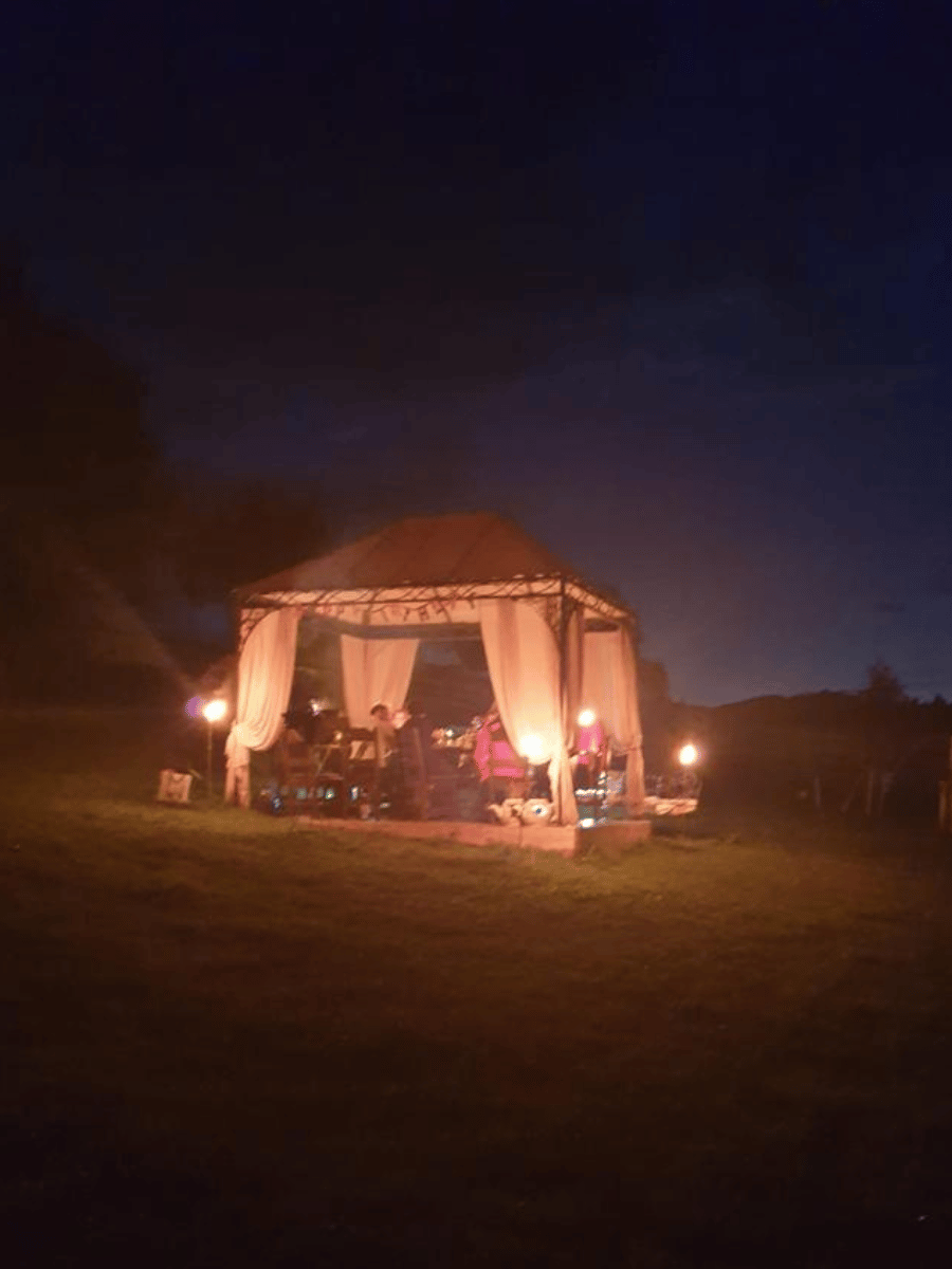 Foișor luminat noaptea cu oaspeți la masă și torțe pe iarbă, Întorsura Buzăului