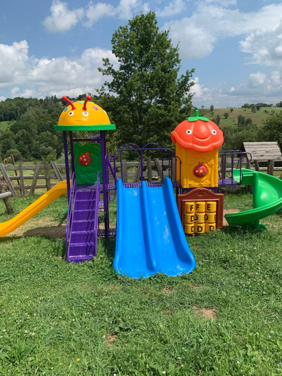 Complex de joacă cu tobogane galben, albastru și spirală verde pe gazon