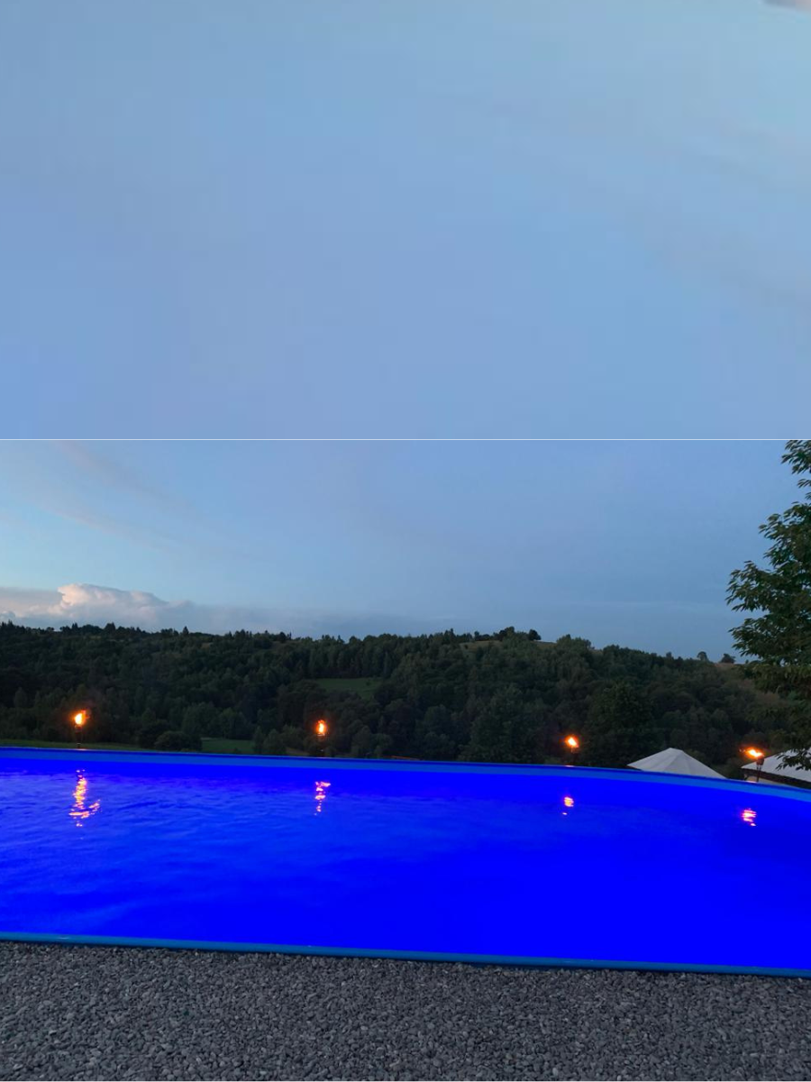 Piscina luminată albastru intens la amurg, cu torțe pe mal la Casa Brădet