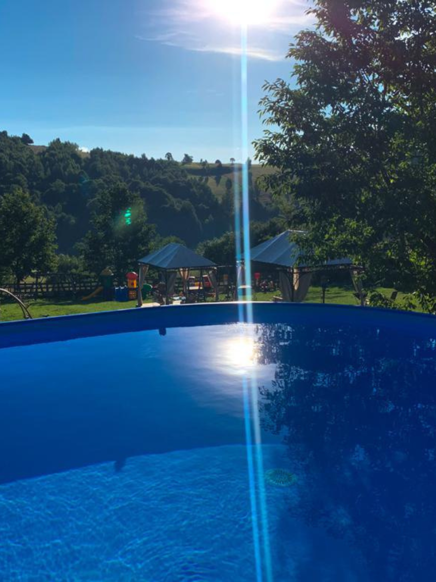 Apă albastră a piscinei, foișoare pe gazon și dealuri verzi în fundal