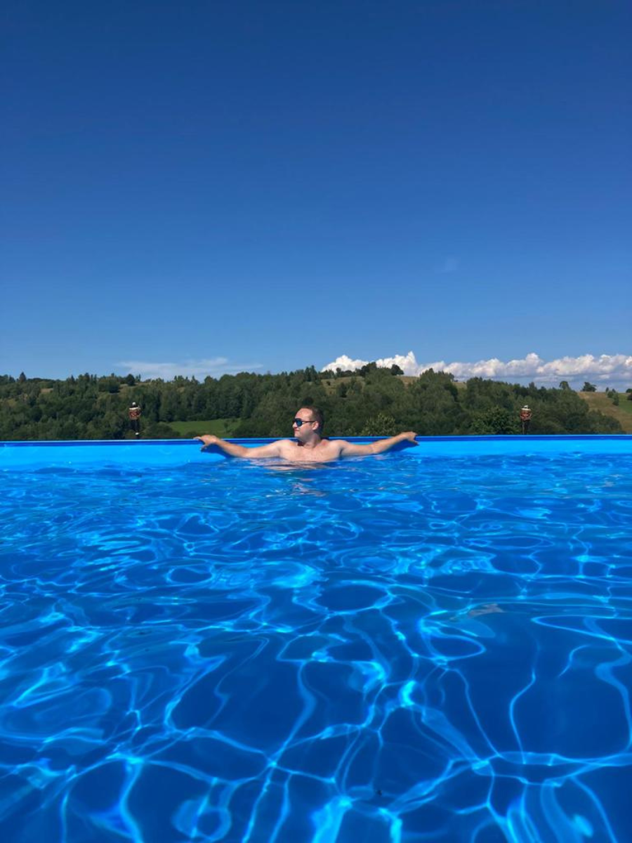 Oaspete relaxat la marginea piscinei, cu dealuri verzi pe fundal