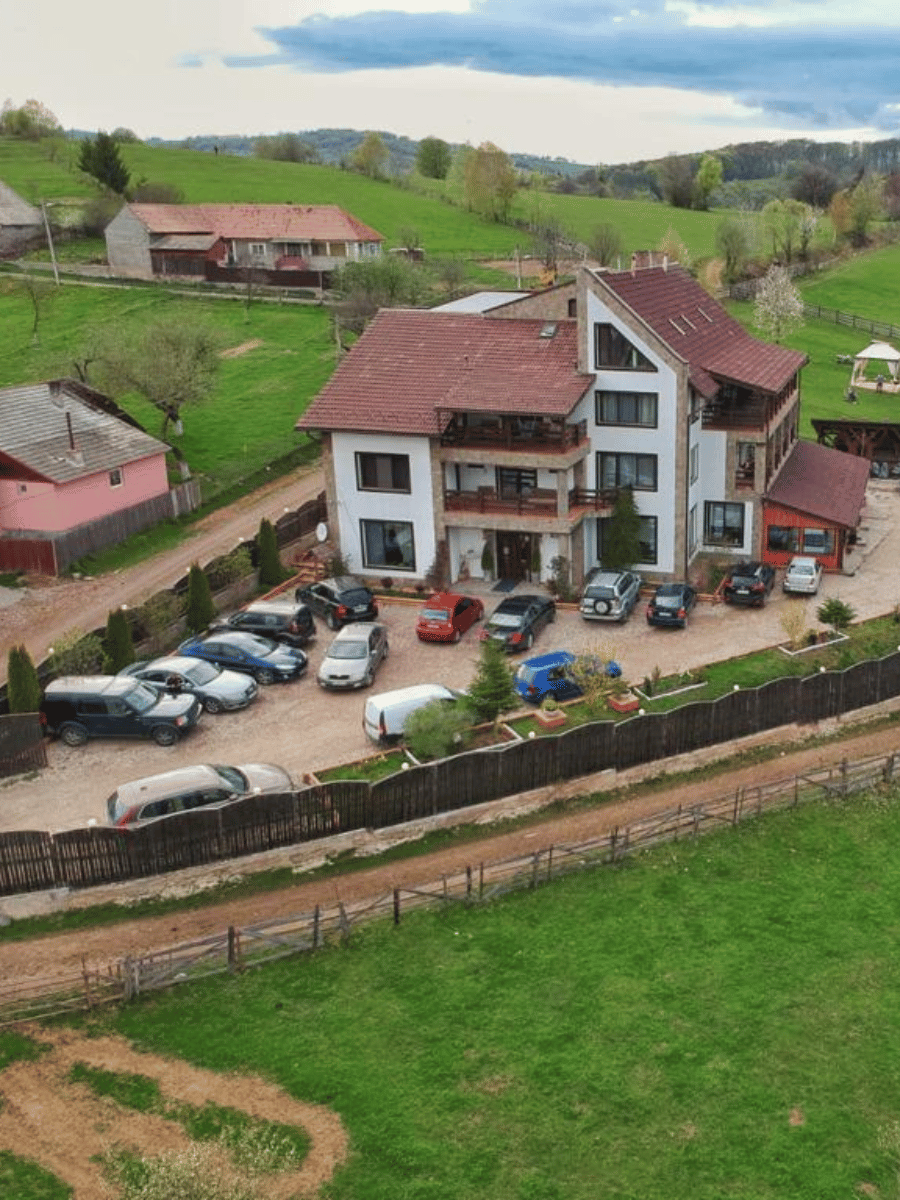 Pensiunea Casa Brădet cu acoperiș roșu și balcoane din lemn, văzută de sus pe peisaj montan