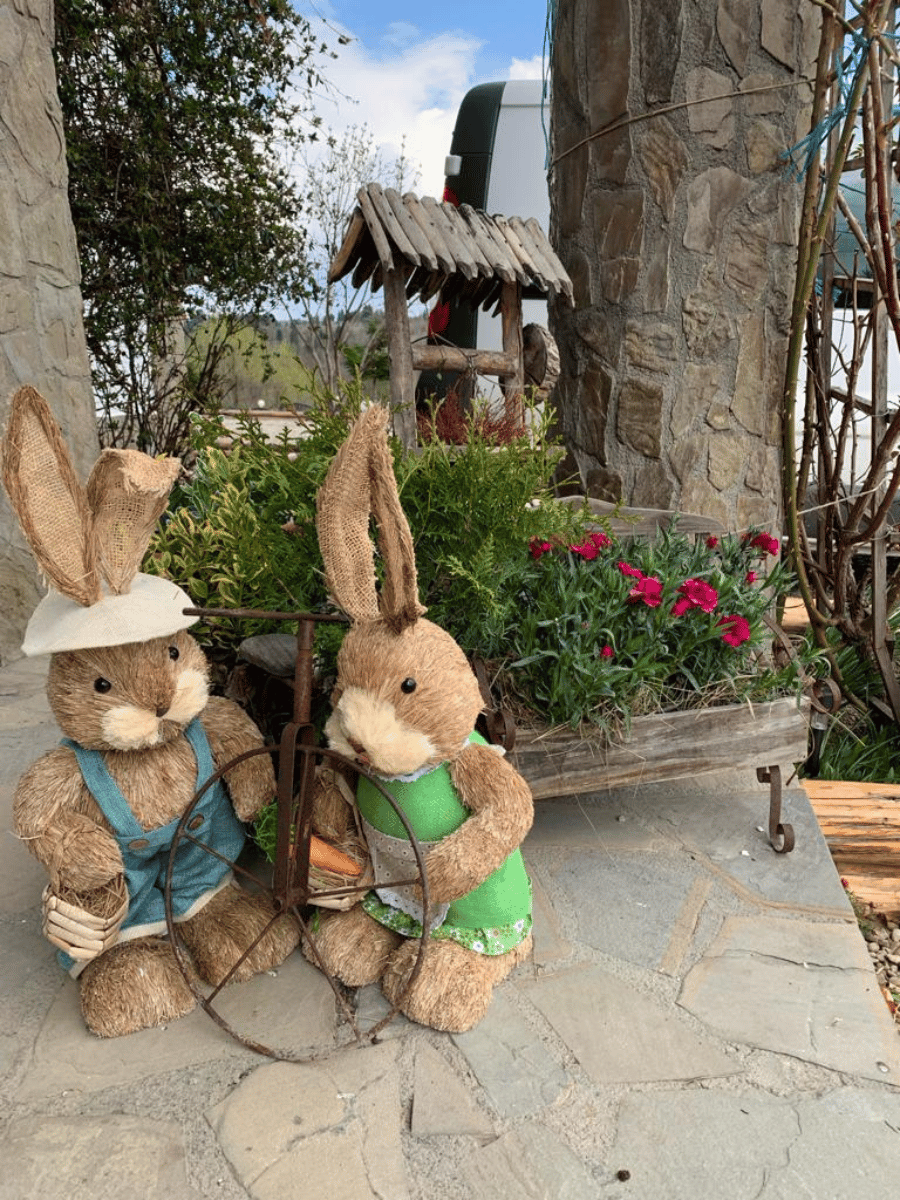 Figurine de iepuri de Paște pe terasa de piatră, lângă jardiniere cu flori