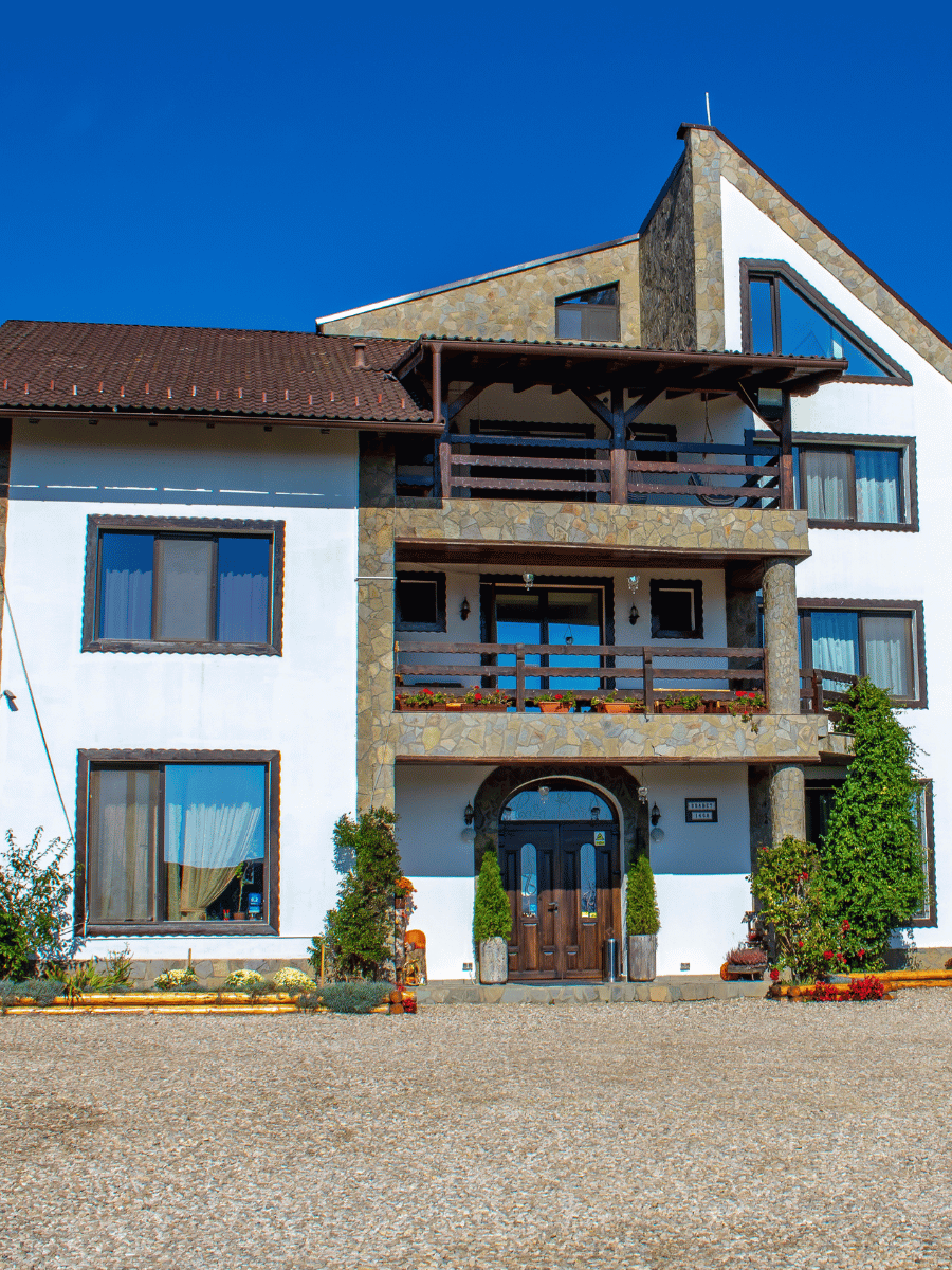Fațada Casa Brădet cu piatră, balcoane din lemn și mușcate roșii, pe cer senin de vară