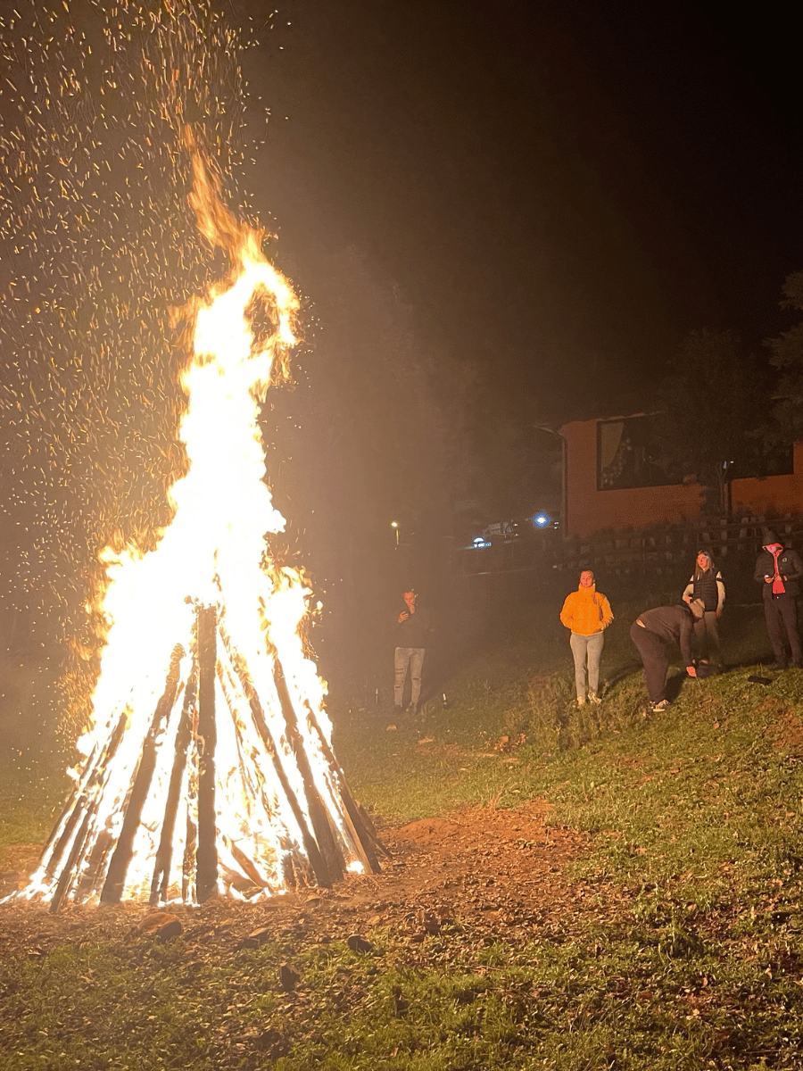 Foc de tabără din bârne pe iarbă, oaspeți privind flăcările la Casa Brădet