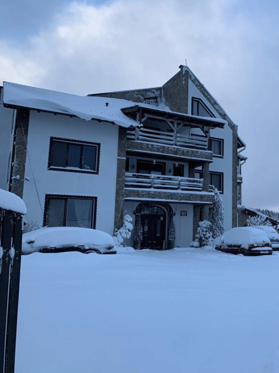 Pensiunea Casa Brădet acoperită de zăpadă, fațadă cu balcoane și peisaj de iarnă la Întorsura Buzăului